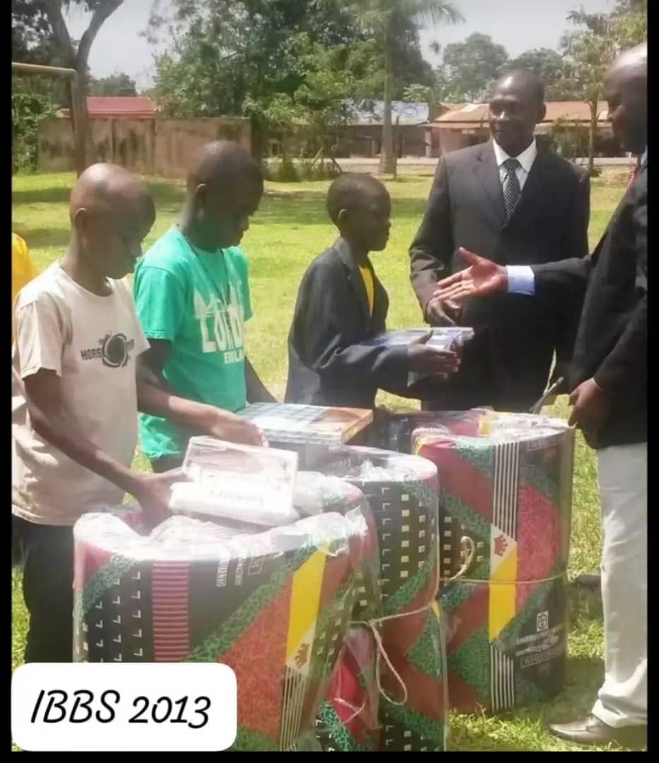 Children collecting gift packages from men in suits at an outdoor award-giving event in 2013