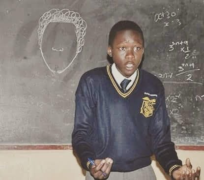 A student in school uniform speaking with his hands in front of a chalkboard