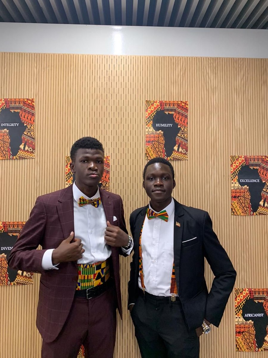 Two young men in suits wearing patterned bow ties in front of a slatted wooden wall